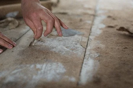 Hände entfernen Teppichkleber mit Spachtel von Holzboden